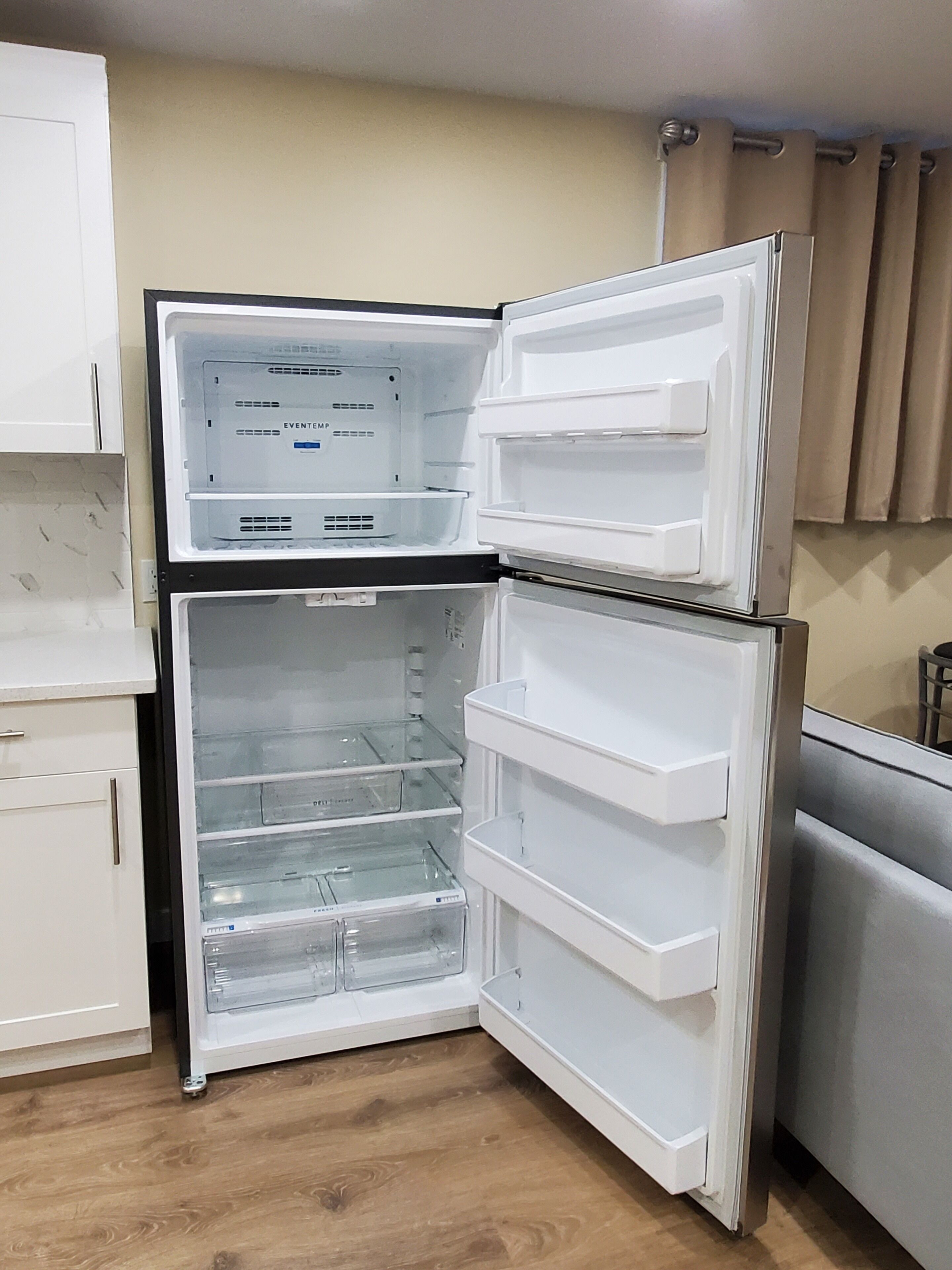 Ein kompakter Kühlschrank mit mehreren Ablagen und einem separaten Gefrierfach, eingebaut in eine Küche mit Holzboden und weißen Schränken.