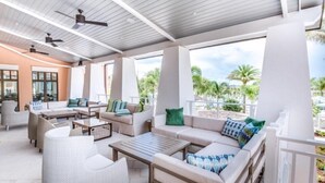 An outdoor patio area with seating arrangements, ceiling fans, and a view of palm trees.