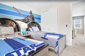 Une chambre avec une couvre-lit aux couleurs de Star Wars, une affiche de Dark Vador et une pancarte sur laquelle on peut lire : « DANS UNE GALAXIE Lointaine, très lointaine… »