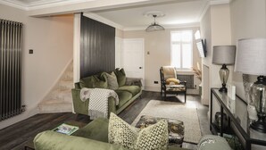 A living room with a green sofa, a patterned rug, and a chair. There is a staircase leading to another room. - 15 Rosemary Lane (Beaumaris)