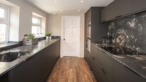 A modern kitchen with dark cabinetry, a marble countertop, and a wooden floor. - 15 Rosemary Lane (Beaumaris)