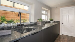 A modern kitchen with a dark countertop, a black faucet, and potted plants. - 15 Rosemary Lane (Beaumaris)
