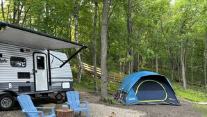 Kampeeropstelling met een caravan, een blauwe tent en een vuurkuil.