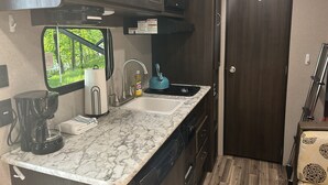Een kleine keuken met een spoelbak, waterkoker en koffiezetapparaat.