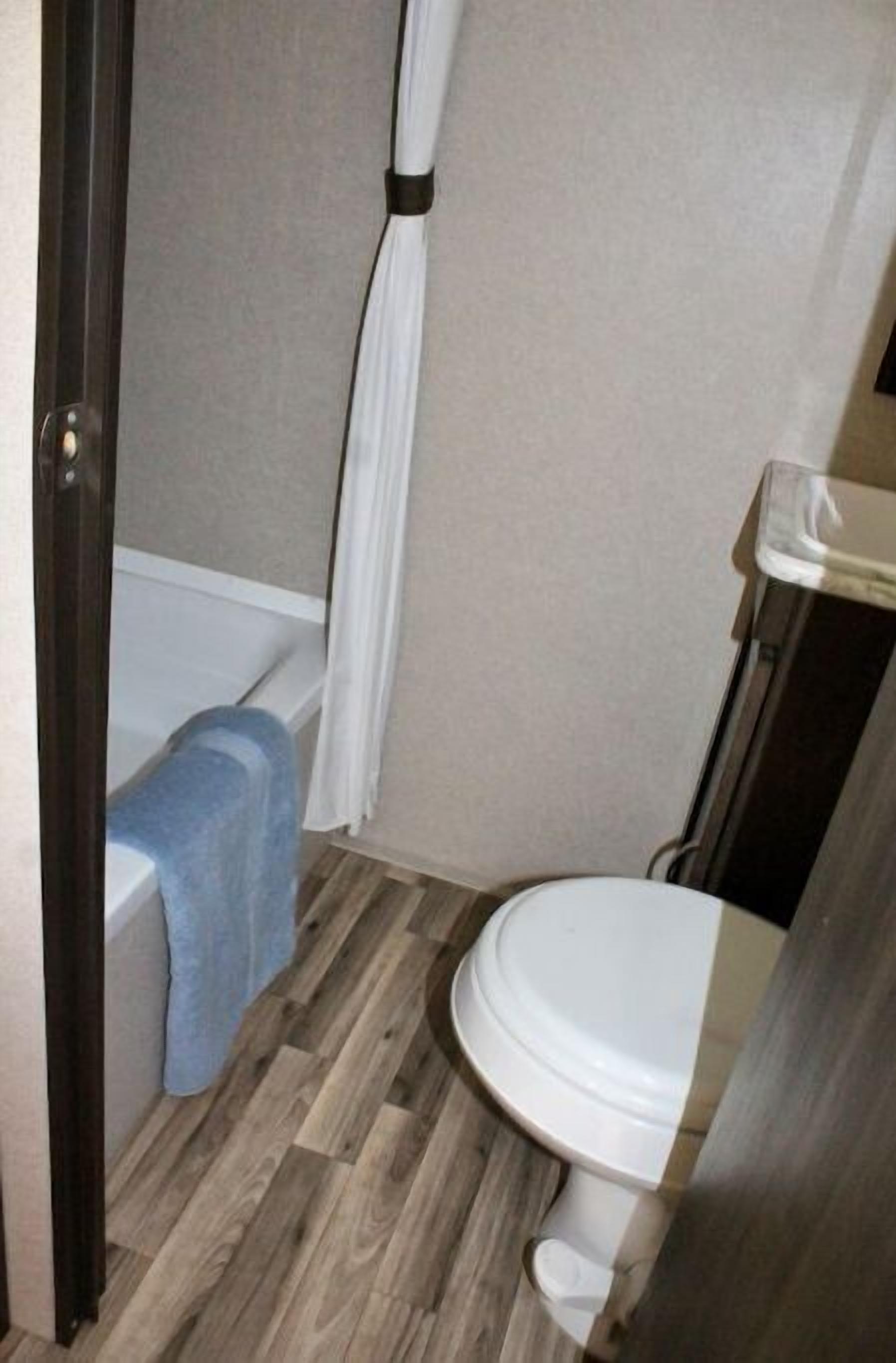 Un baño con piso de madera, una bañera blanca y un inodoro blanco.