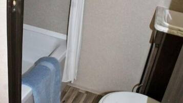 Un baño con piso de madera, una bañera blanca y un inodoro blanco.