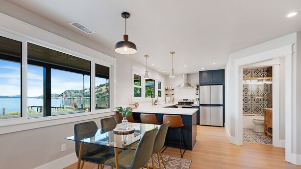 A modern kitchen with a large island, a dining area with a glass table, and a view of the lake. - Silverado Beach Lake House (Clearlake)