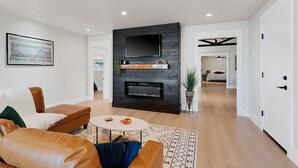 A modern living room with a fireplace, leather sofas, a flat-screen TV, and a dining area with a patterned rug. - Silverado Beach Lake House (Clearlake)