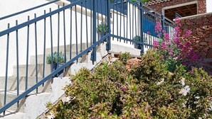 Una escalera con barandilla azul que lleva a un edificio de fachada de piedra y un pequeño jardín con flores rosadas.