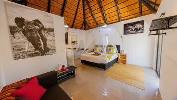 A bedroom with a bed, a nightstand, a bedside table, a chair, a sofa, a wall-mounted TV, and a ceiling fan.