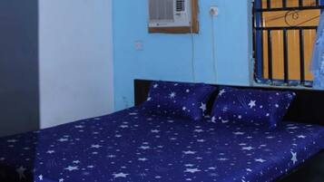 A bedroom with a bed, a ceiling fan, a window with bars, and an air conditioning unit.