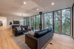 Relax in this stylish living room with a large sofa, glass coffee table, and fireplace, offering a view of the surrounding forest.
