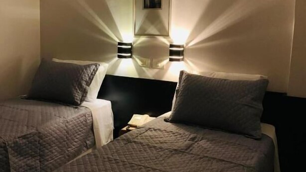 A hotel room with two beds, a headboard, and wall-mounted lighting.