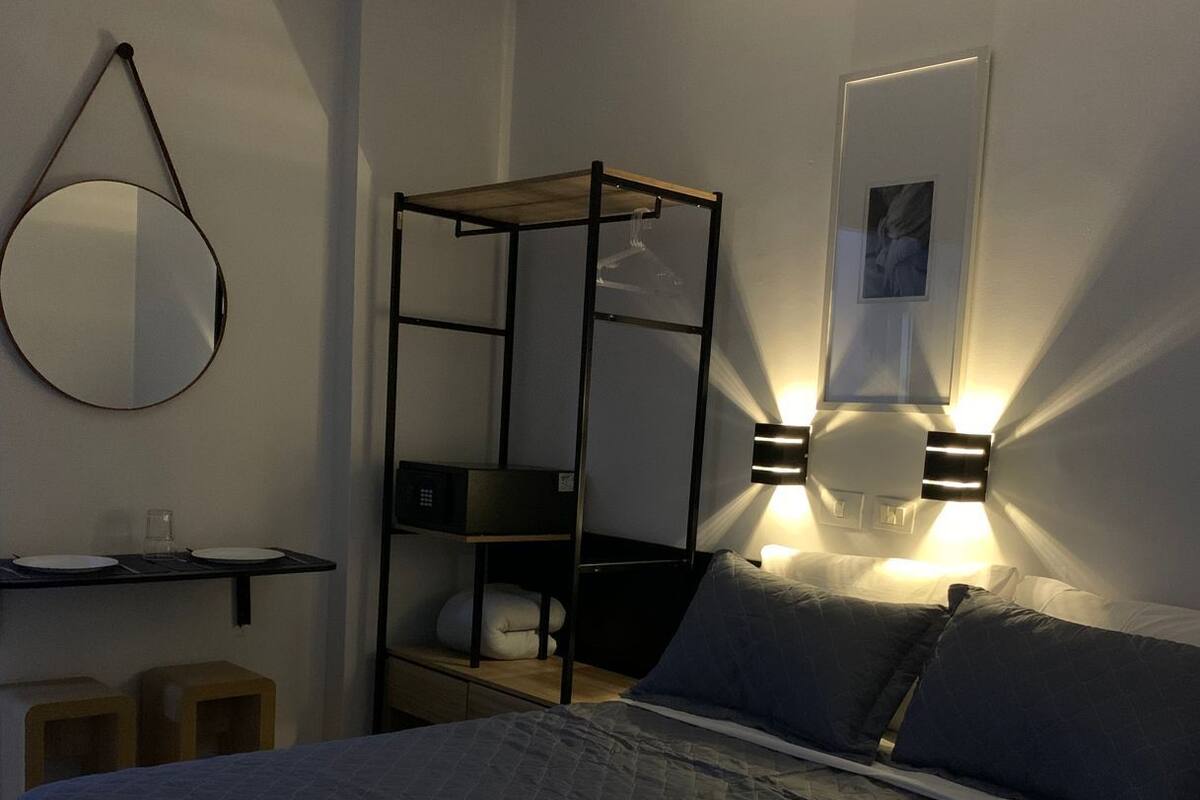 Un dormitorio con una cama, una lámpara colgante, un estante y un cuadro en la pared.