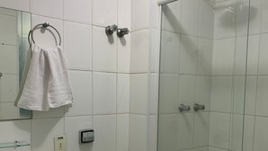 A bathroom with white tiles, a glass shower enclosure, a sink, and a toilet.