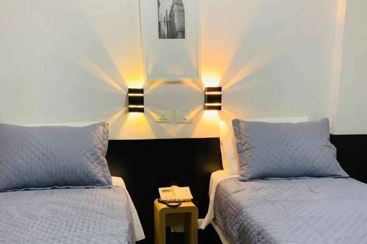 Una habitación con dos camas, un taburete pequeño y luces en la pared.
