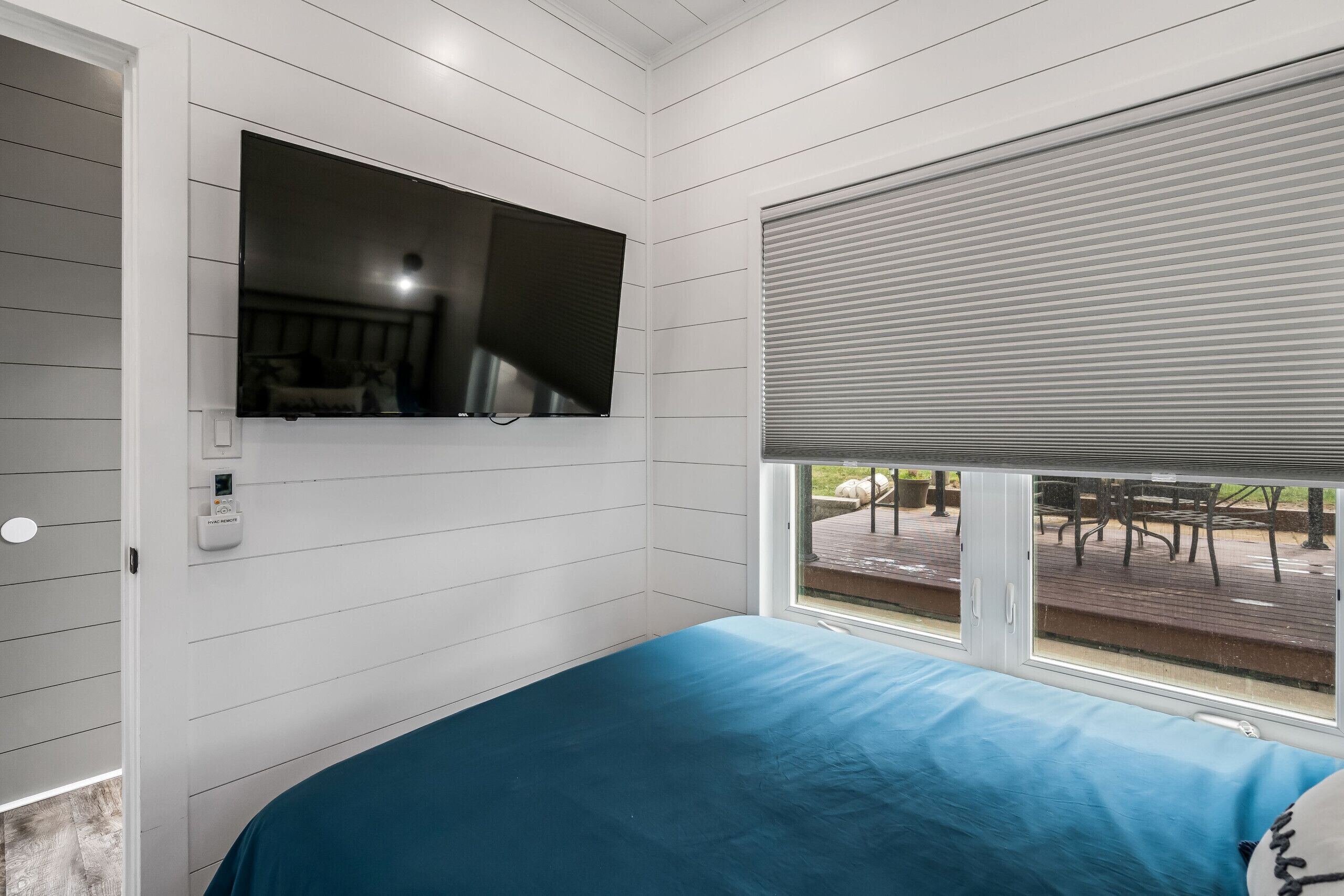 A bedroom with a bed, a mounted TV, and a window with blinds.