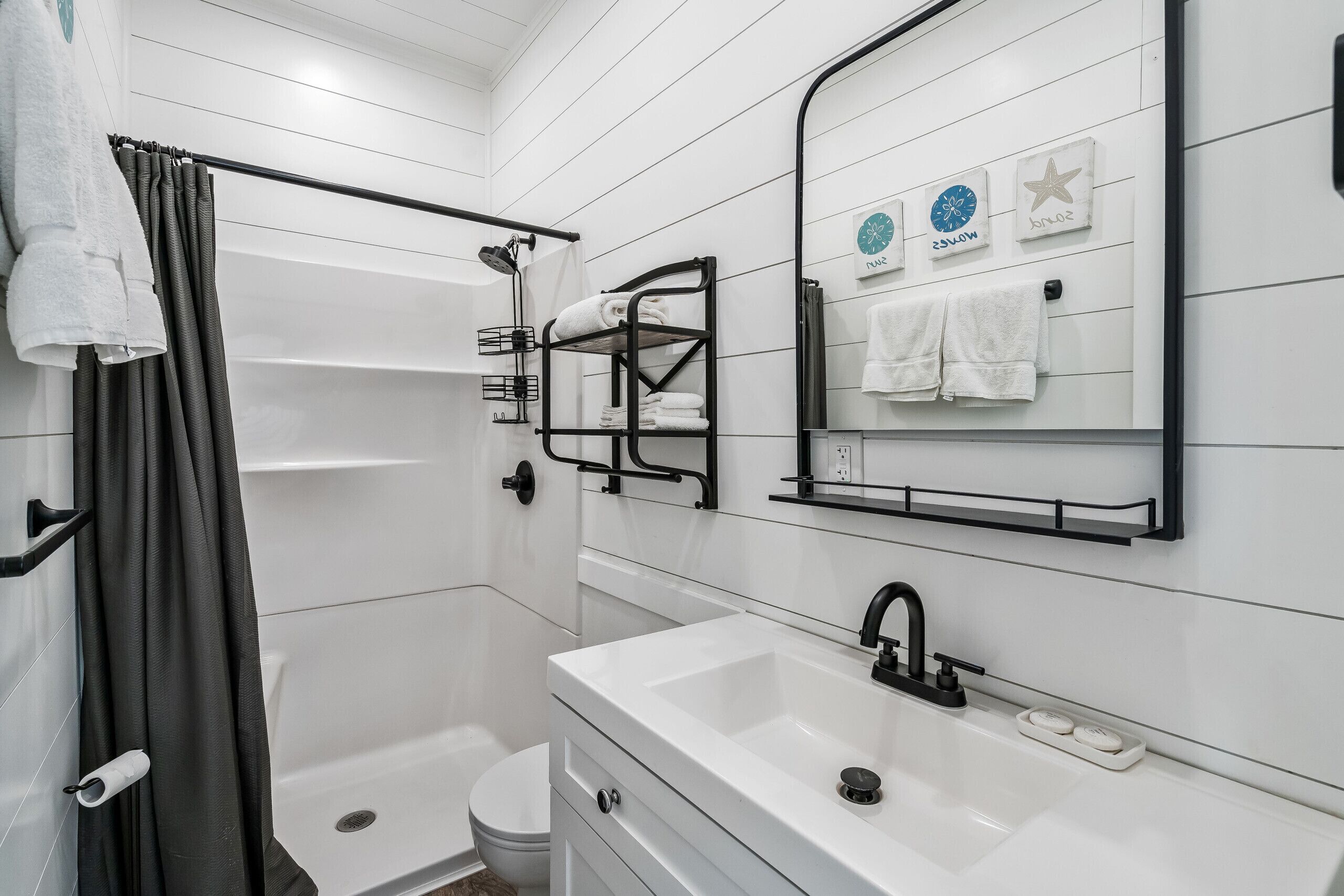 A modern bathroom with a shower, toilet, and sink. There are towels hanging on a rack and a towel bar.