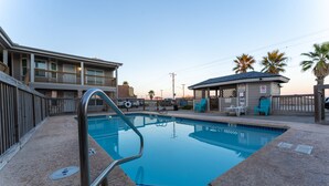 A swimming pool with a metal ladder, surrounded by a fence, and a building with a balcony in the background.