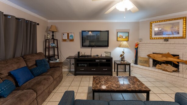 A living room with a ceiling fan, a TV, a fireplace, and a couch with blue cushions. - SA7 Family-Friendly Condo: Waterfront-Complex, Pool, Walk to the Beach, Fishing (Corpus Christi)