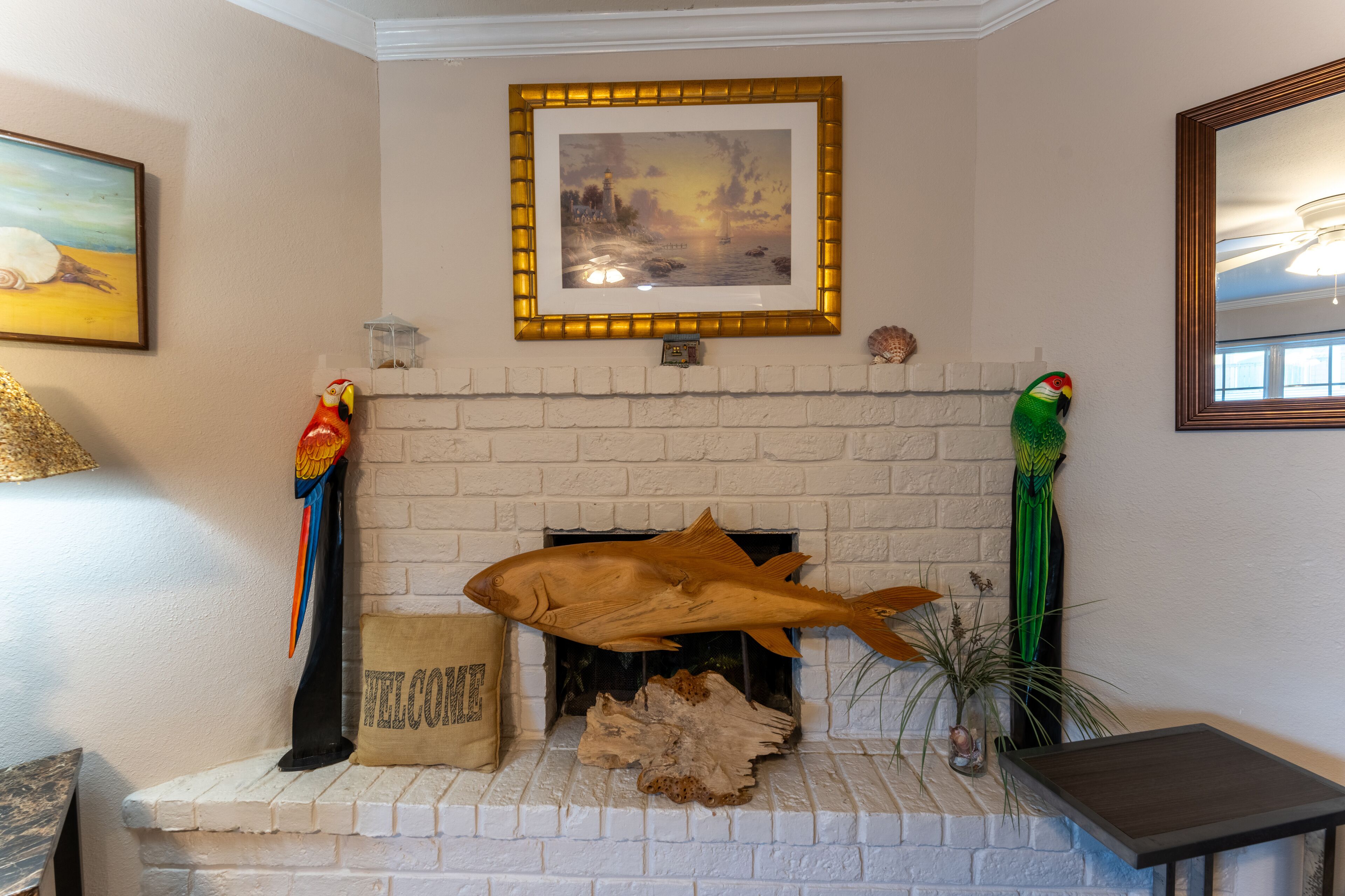 Una chimenea con una gran decoración de pez, un cuadro enmarcado encima y un loro en la pared.