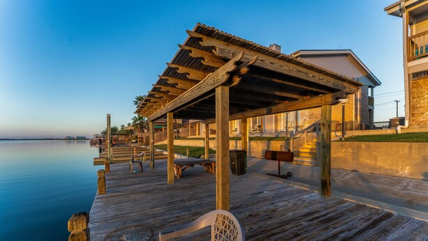 A wooden pier extending into calm water, with a covered seating area and a building adjacent to it.