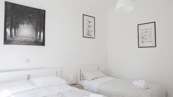 Habitación de hotel minimalista con dos camas, un cuadro grande enmarcados con un sendero forestal y dos cuadros más pequeños en las paredes.