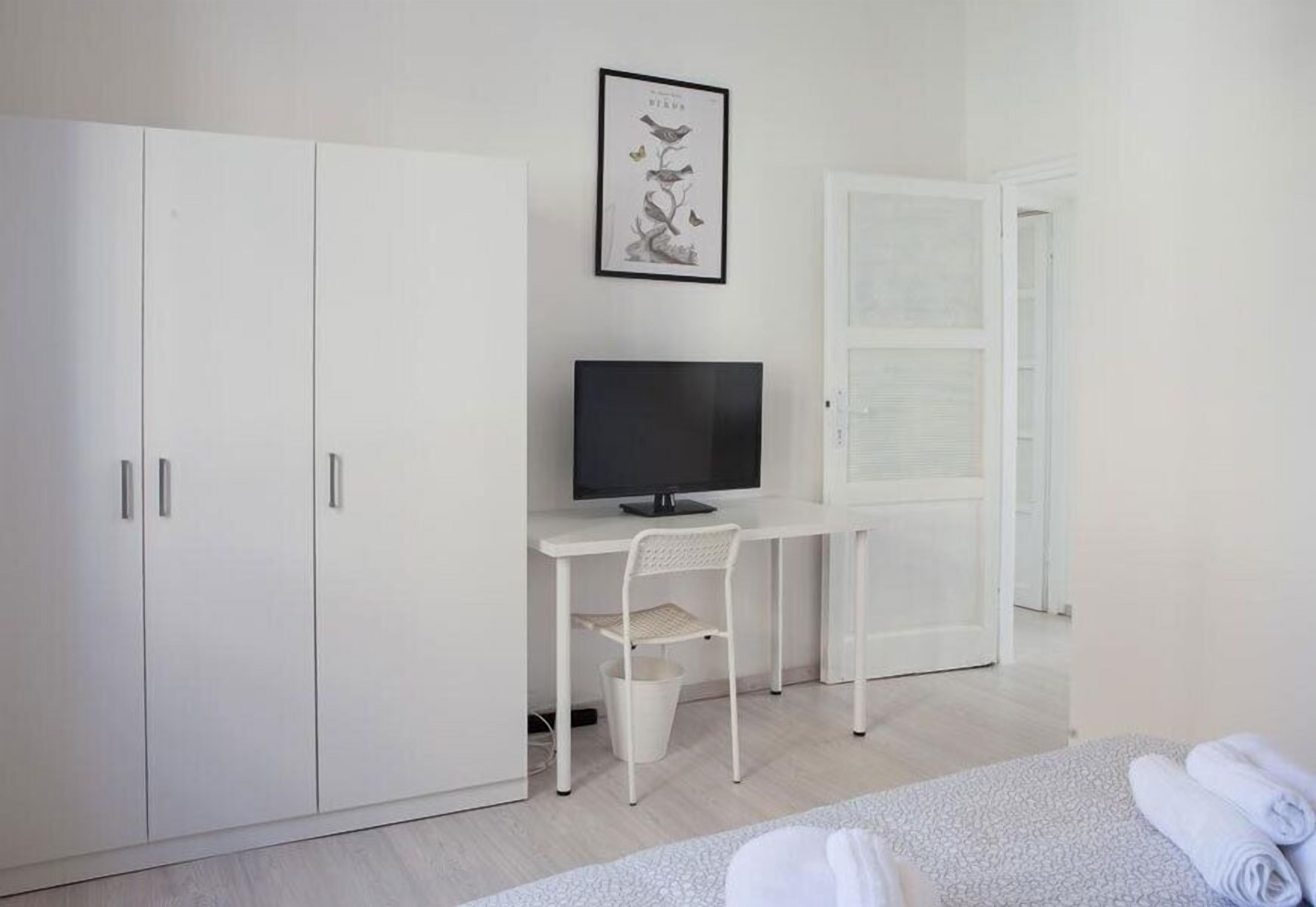 Una habitación minimalista con cama, escritorio con computadora, televisor y armario.