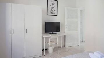 Una habitación minimalista con cama, escritorio con computadora, televisor y armario.