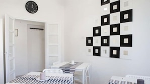 A hotel room with a checkered tablecloth, a clock on the wall, and a patterned wall decoration. - Cleo Giglio  (Ancona)