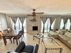 Ein Wohnzimmer mit Kamin, Deckenventilator, Esstisch mit Stühlen und einer Couch.