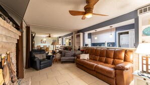 A living room with a brown leather sofa, a black leather couch, and a grey armchair. There is a ceiling fan, a lamp, and a white cabinet in the background. - Waterfront Condo: Stunning Sunsets, Fishing, Patio, & 4 minutes from the beach!  (Corpus Christi)