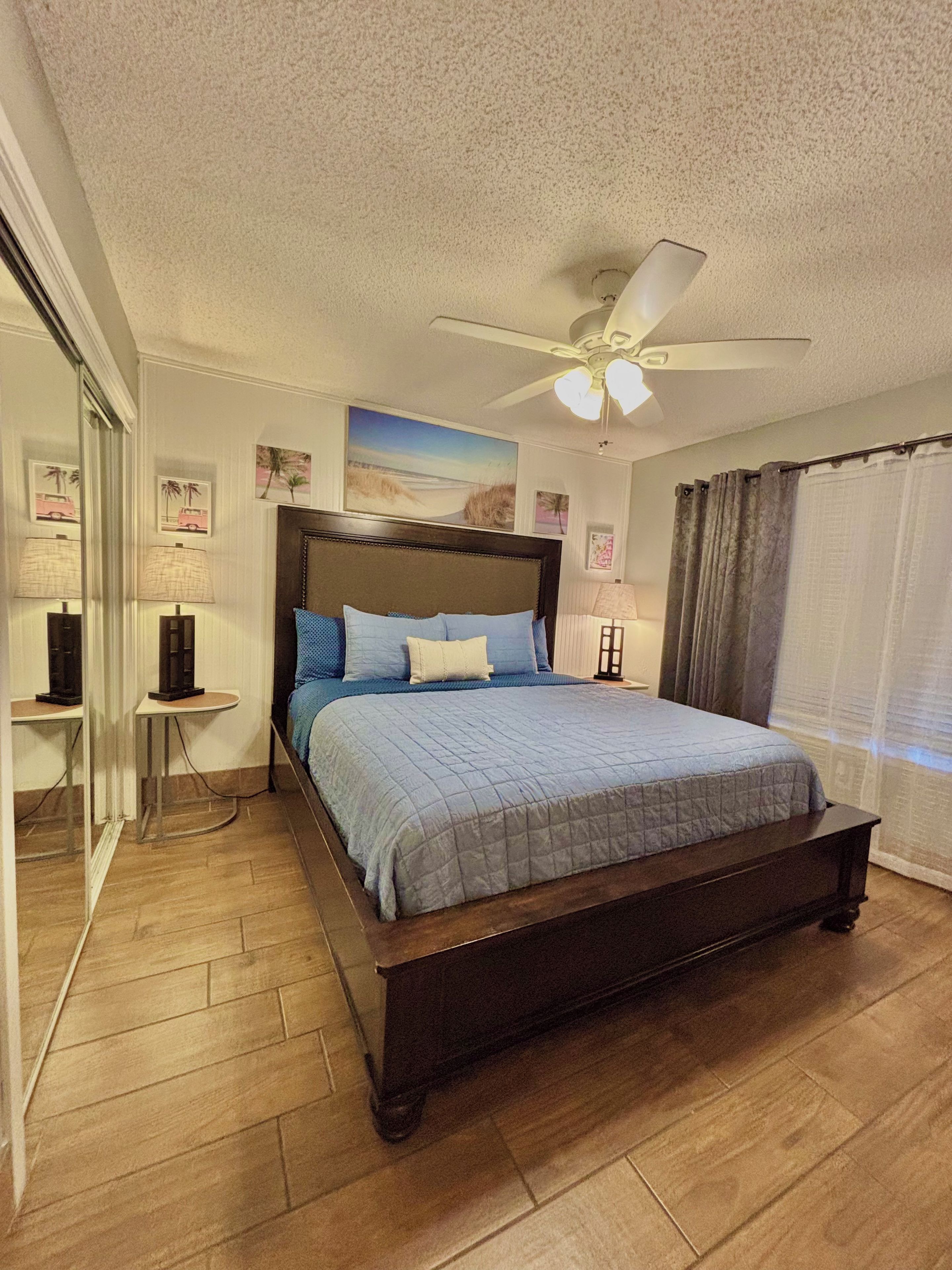 A bedroom with a large bed, a ceiling fan, and a window with curtains.