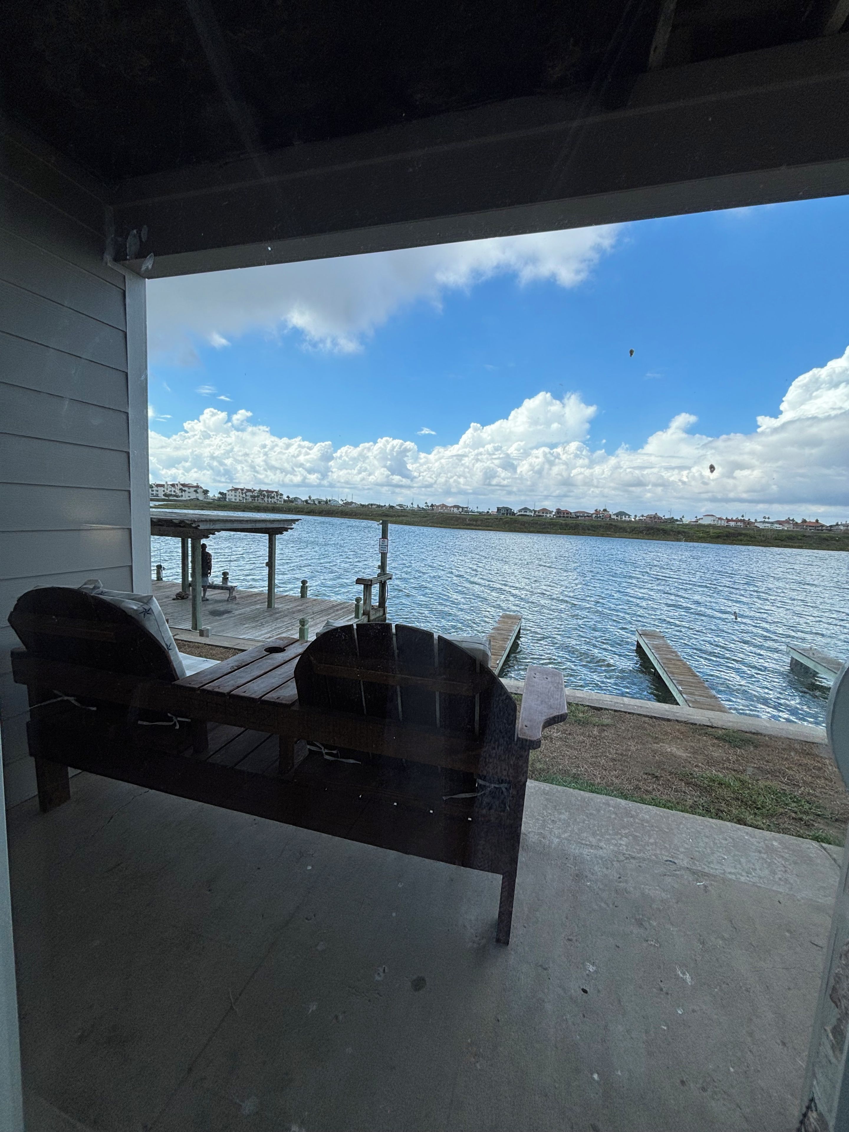 Un banco de madera en un patio de concreto con vista a un cuerpo de agua, un muelle y un cielo despejado.