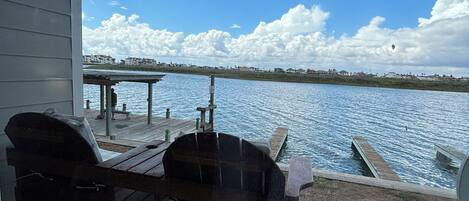 Un banco de madera en un patio de concreto con vista a un cuerpo de agua, un muelle y un cielo despejado.