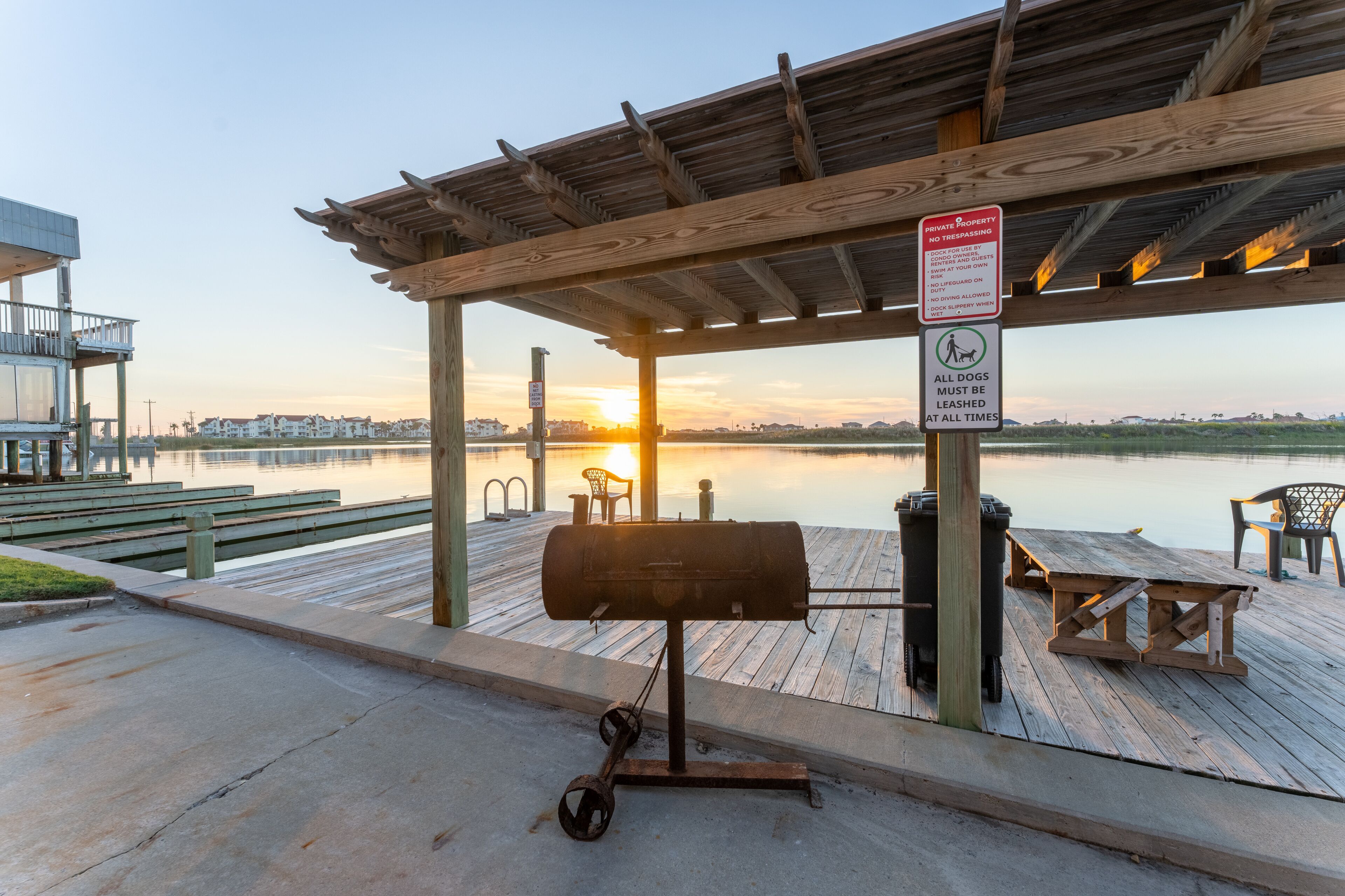 A wooden deck with a grill, picnic tables, and benches overlooking a body of water.