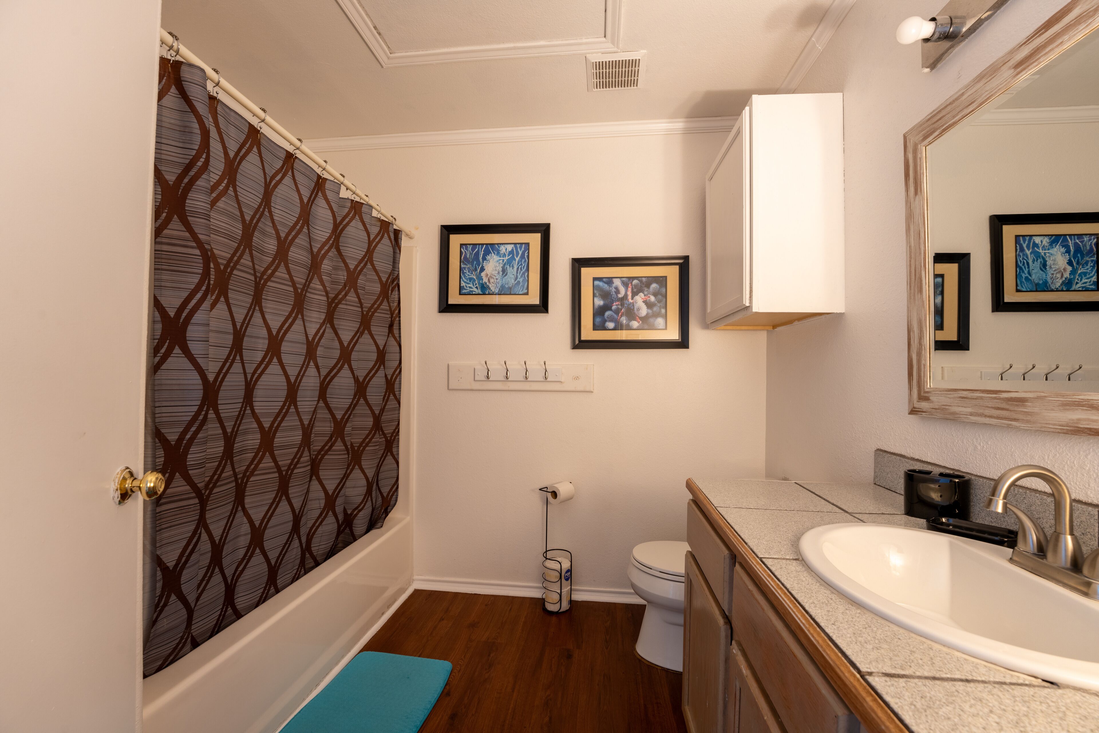 A bathroom with a shower, toilet, sink, and framed artwork on the wall.