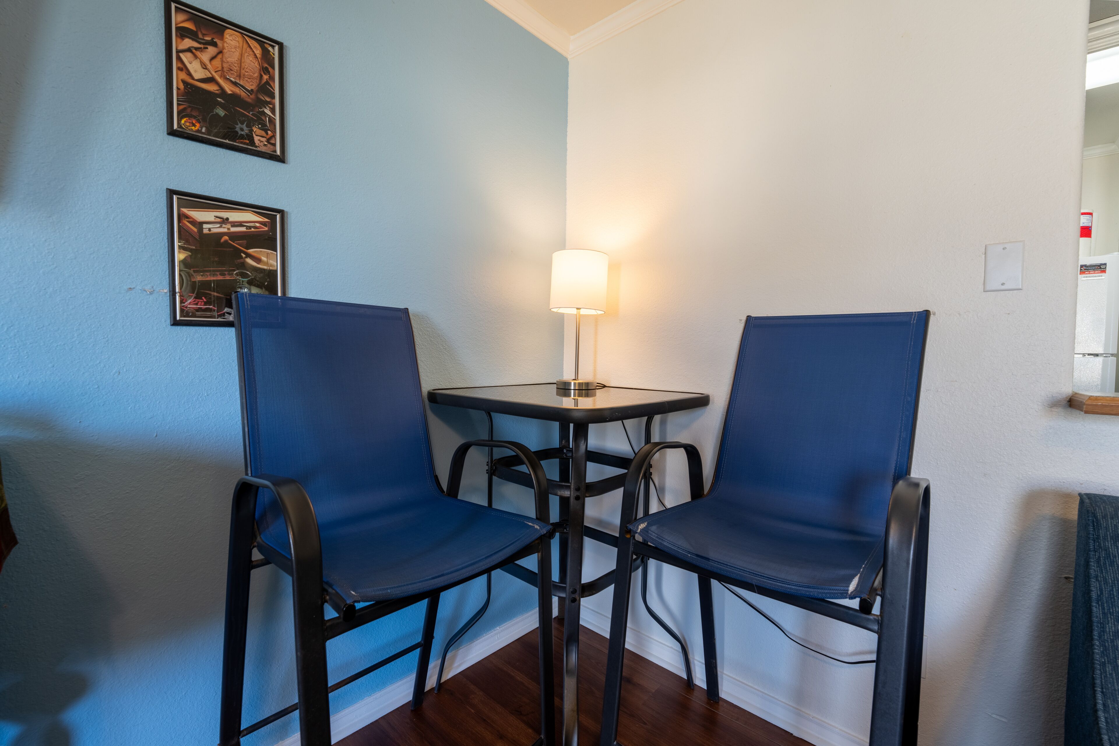 A corner room with two blue chairs, a small table, and a wall-mounted lamp.