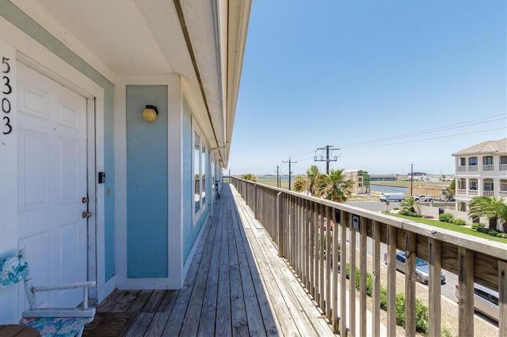 Un balcon en bois offrant une vue sur une plage et un immeuble situé de l’autre côté de la rue.