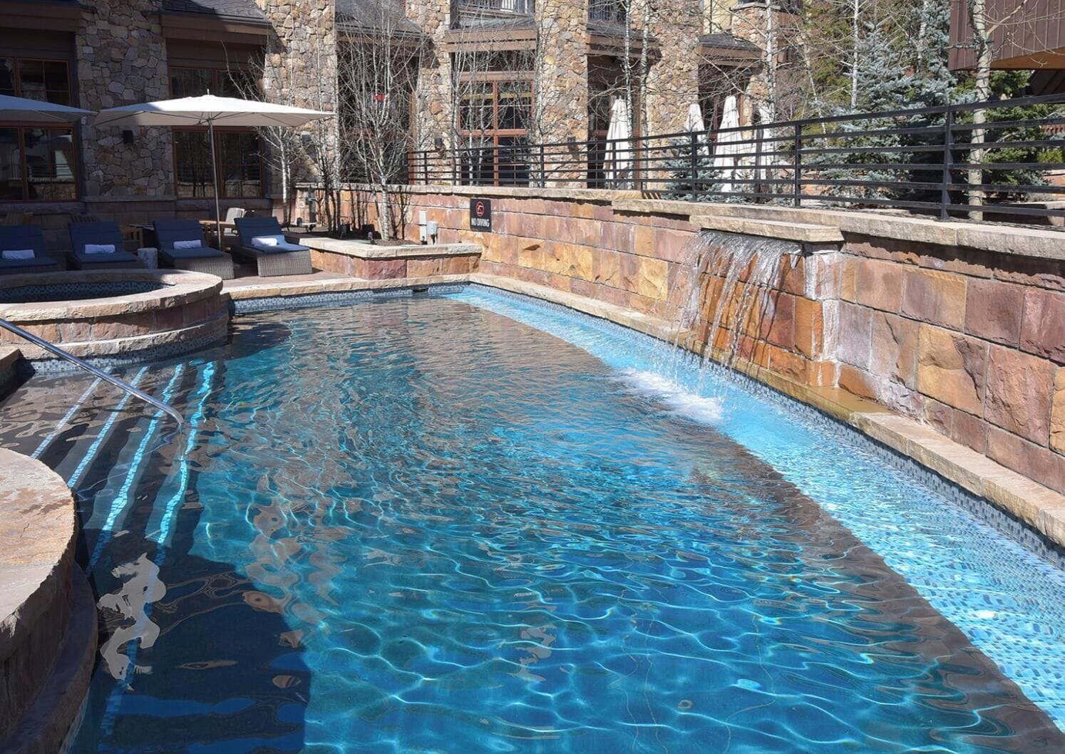 A clear swimming pool with a stone wall and a waterfall feature.