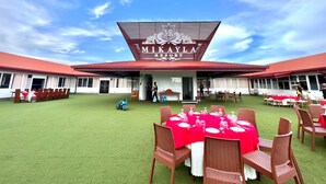 A resort with a red roof and a sign reading "MIKAYLA RESORT". There are tables set up outdoors with chairs, and a person is visible near the entrance. - Mikayla Resort (Chilaw)
