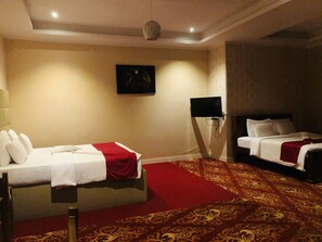 A hotel room with two beds, a red carpet, a painting on the wall, and a television mounted on the wall. - Mikayla Resort (Chilaw)