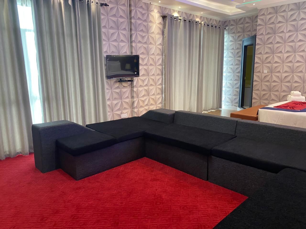 A modern hotel room with a sectional sofa, a flat-screen TV, and a red carpet.
