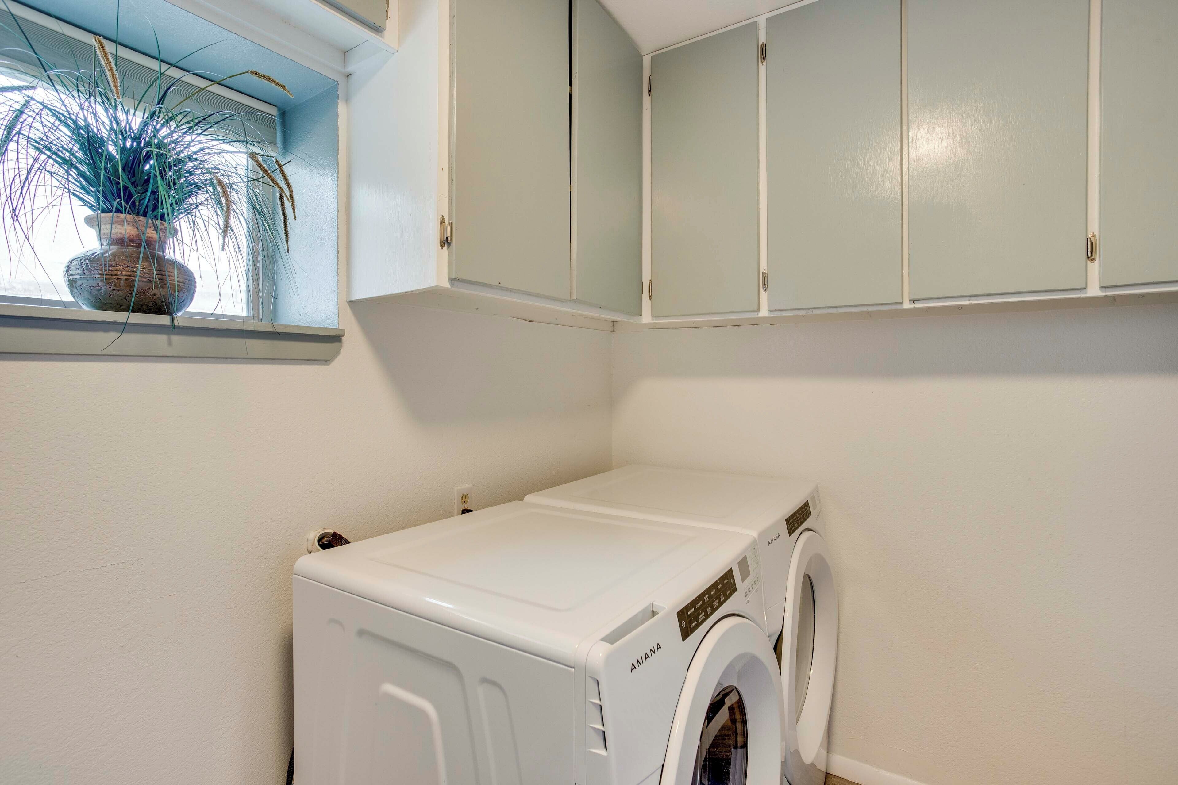 Une buanderie équipée d’un lave-linge à chargement frontal, d’une plante en pot près de la fenêtre et de meubles de couleur claire.