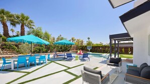A backyard with a swimming pool, blue lounge chairs, and umbrellas.