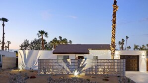 A modern house with a white exterior, a dark roof, and a decorative fence with lights.