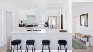 A modern kitchen with white cabinets, a central island with stools, a refrigerator, and a microwave.