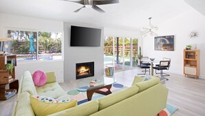 A modern living room with a fireplace, a large TV, and a dining area with outdoor views.