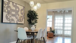Un comedor con una mesa de madera, sillas blancas, una planta en maceta y un cuadro abstracto moderno en la pared.