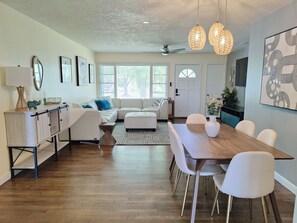 Un salon moderne avec un coin repas, comprenant un canapé, une table basse, une table à manger avec des chaises et des luminaires suspendus.